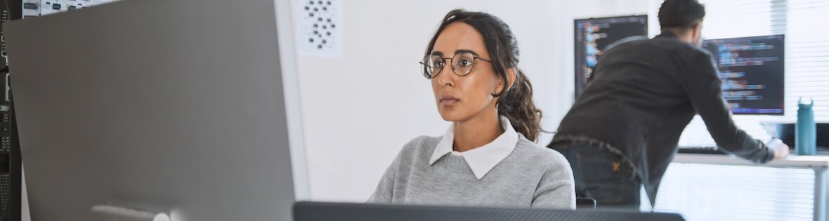 Woman working at a computer screen while a man behind her reviews code.